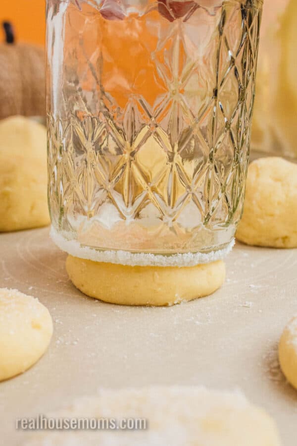 drinking glass bottom coated in sugar flattening a cookie dough scoop on a baking sheet