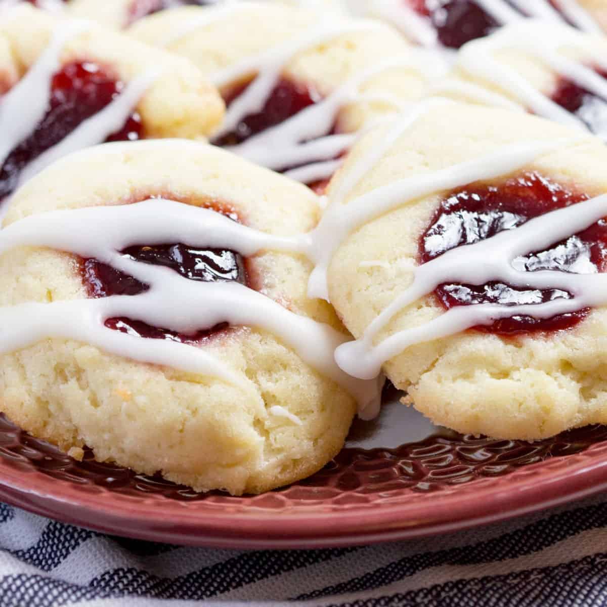 square image of raspberry thumbprint cookies with icing drizzle on a plate