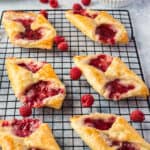 square image of raspberry cheese danishes on a wire rack with fresh raspberries