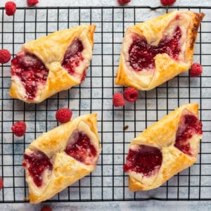 square image of raspberry cheese danishes on a wire rack with fresh raspberries