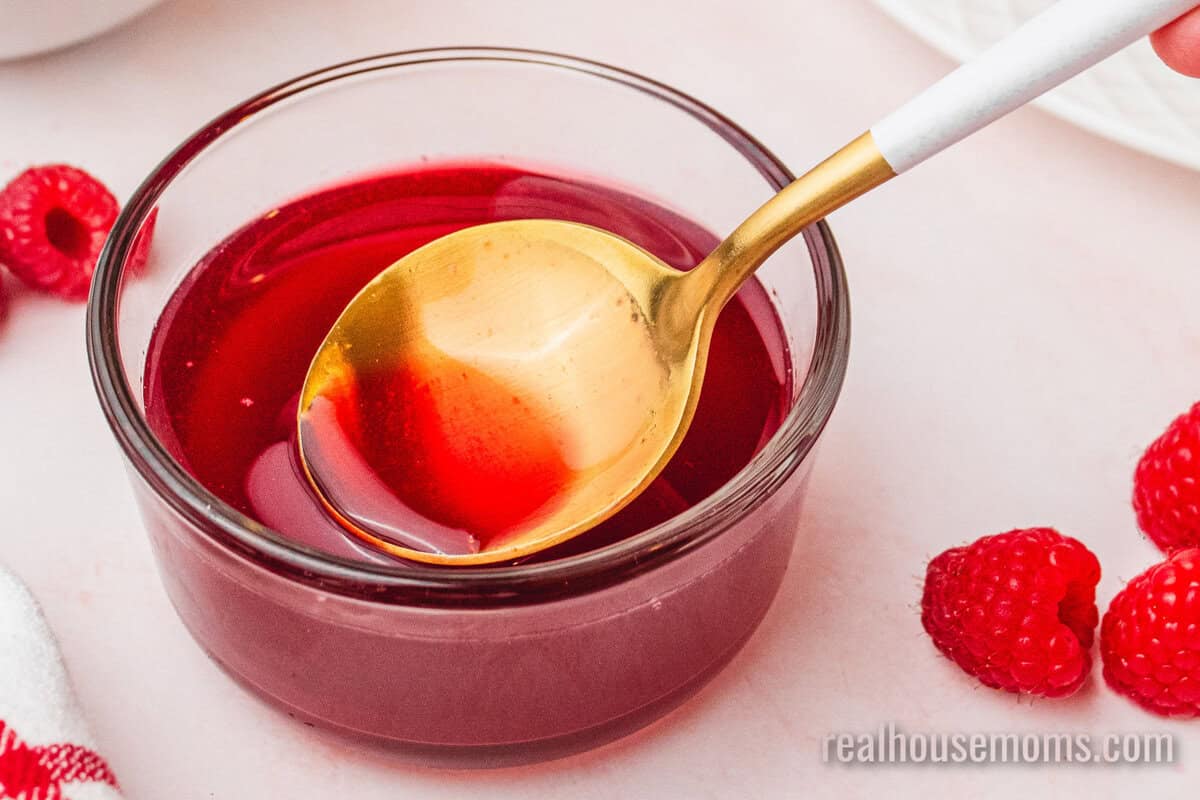 spoon resting in a small bowl of raspberry syrup