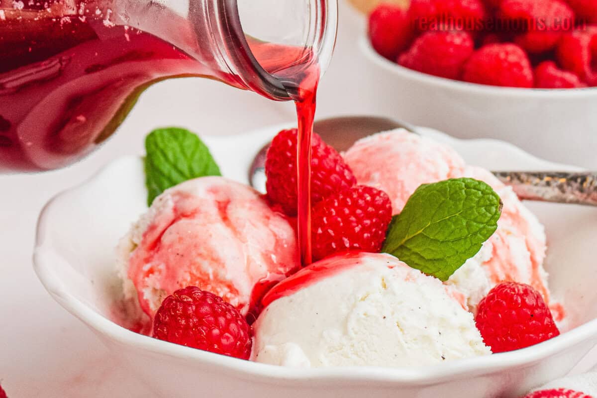 raspberry syrup being poured over scoop of vanilla ice cream and fresh mint in a bowl