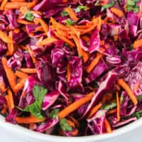 red cabbage slaw in a serving bowl with wooden spoon with recipe name at the bottom