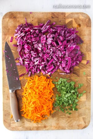 shredded cabbage, shredded carrots, and chopped cilantro on a cutting board with a knife