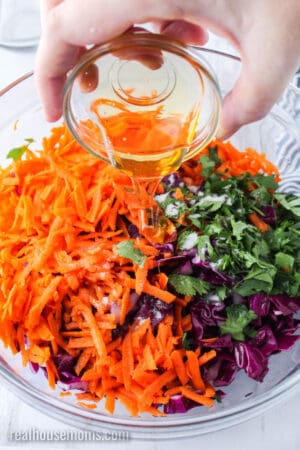 honey being poured over veggies in a bowl for red cabbage slaw