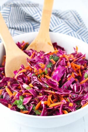 red cabbage slaw in a white serving bowl with wooden spoons