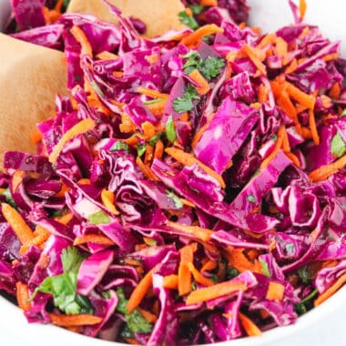 square image of red cabbage slaw in a bowl with wooden spoons