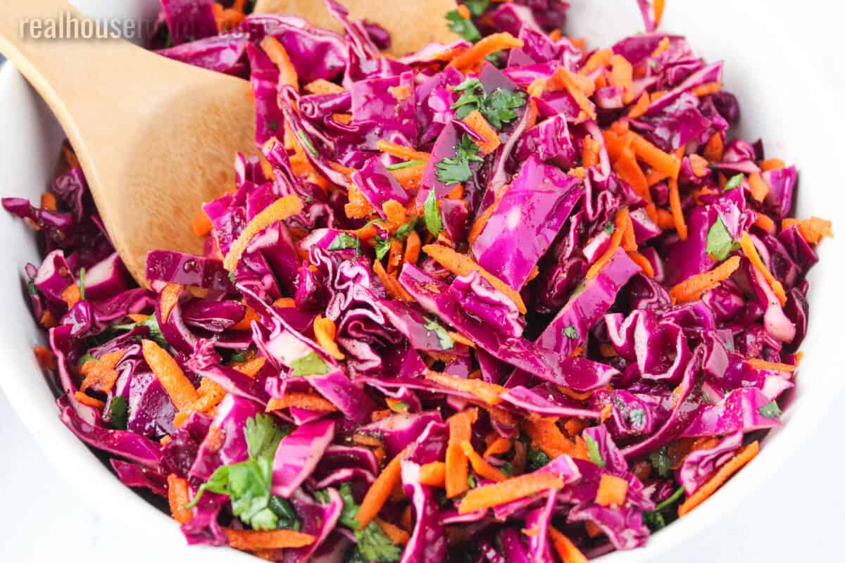 close up of a serving bowl of red cabbage slaw with wooden spoons