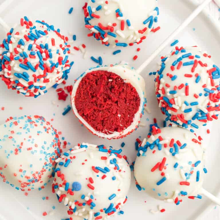 square image of red velvet cake pops on a plate with one cut in half to show the filling