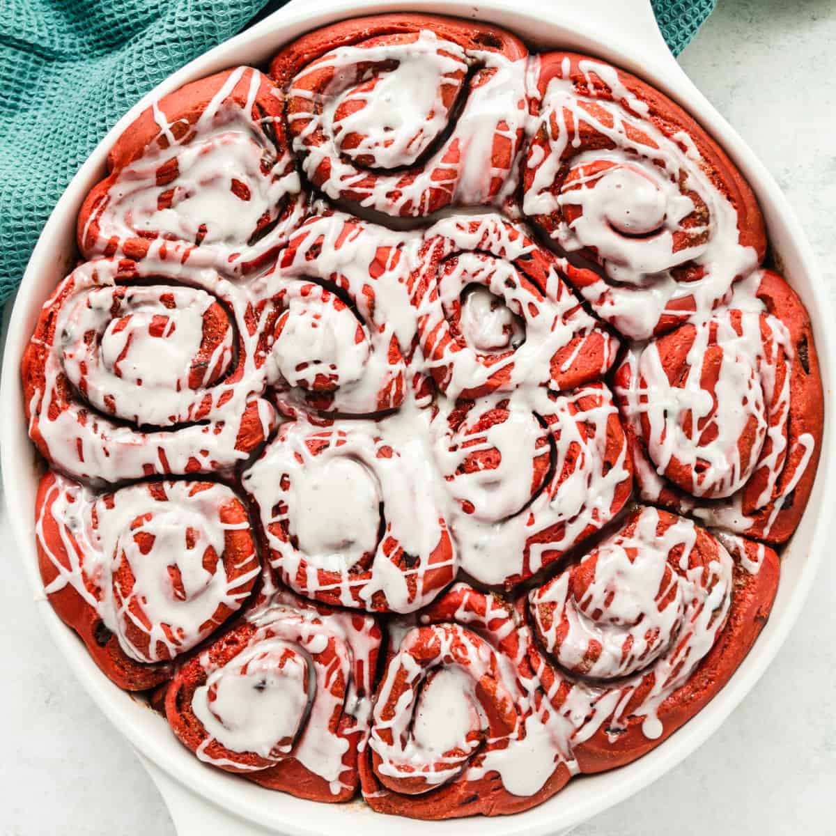 square image of red velvet sweet rolls with icing in a round pan