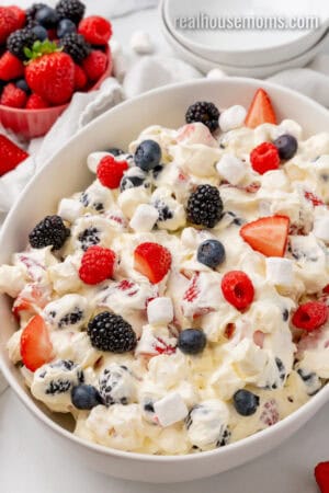 angled view of red white and blue cheesecake salad in a white serving bowl next to a bowl of berries