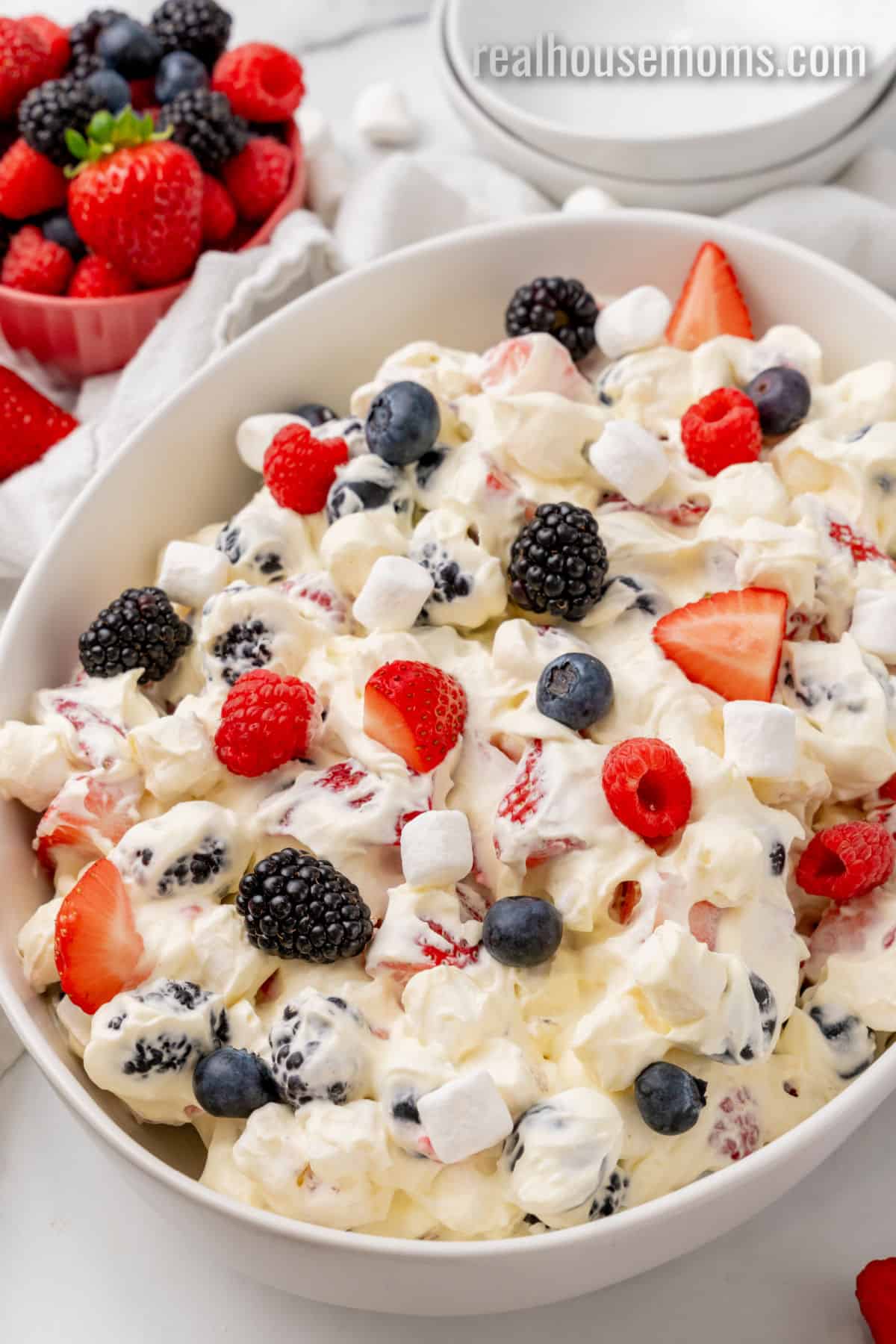 angled view of red white and blue cheesecake salad in a white serving bowl next to a bowl of berries
