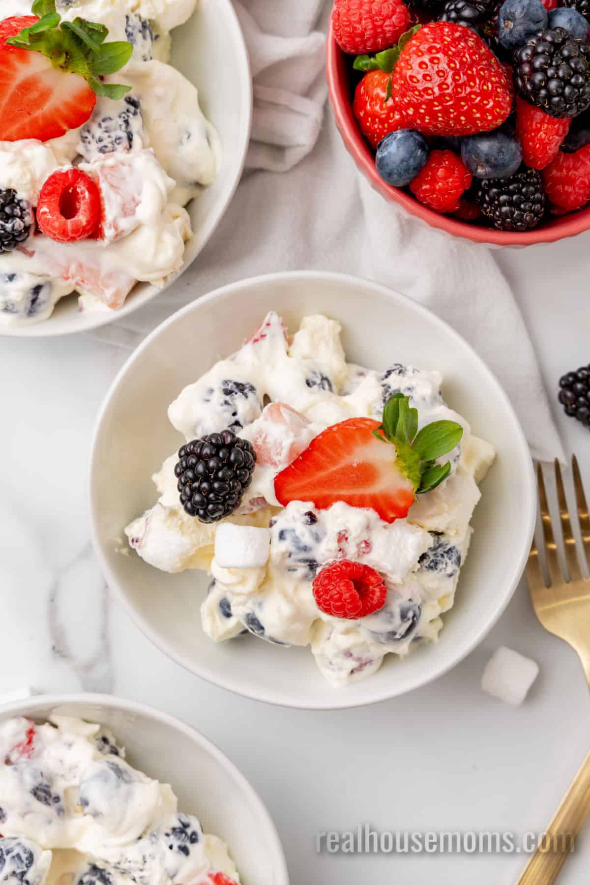 small bowls of red white and blue cheesecake salad topped with half a strawberry