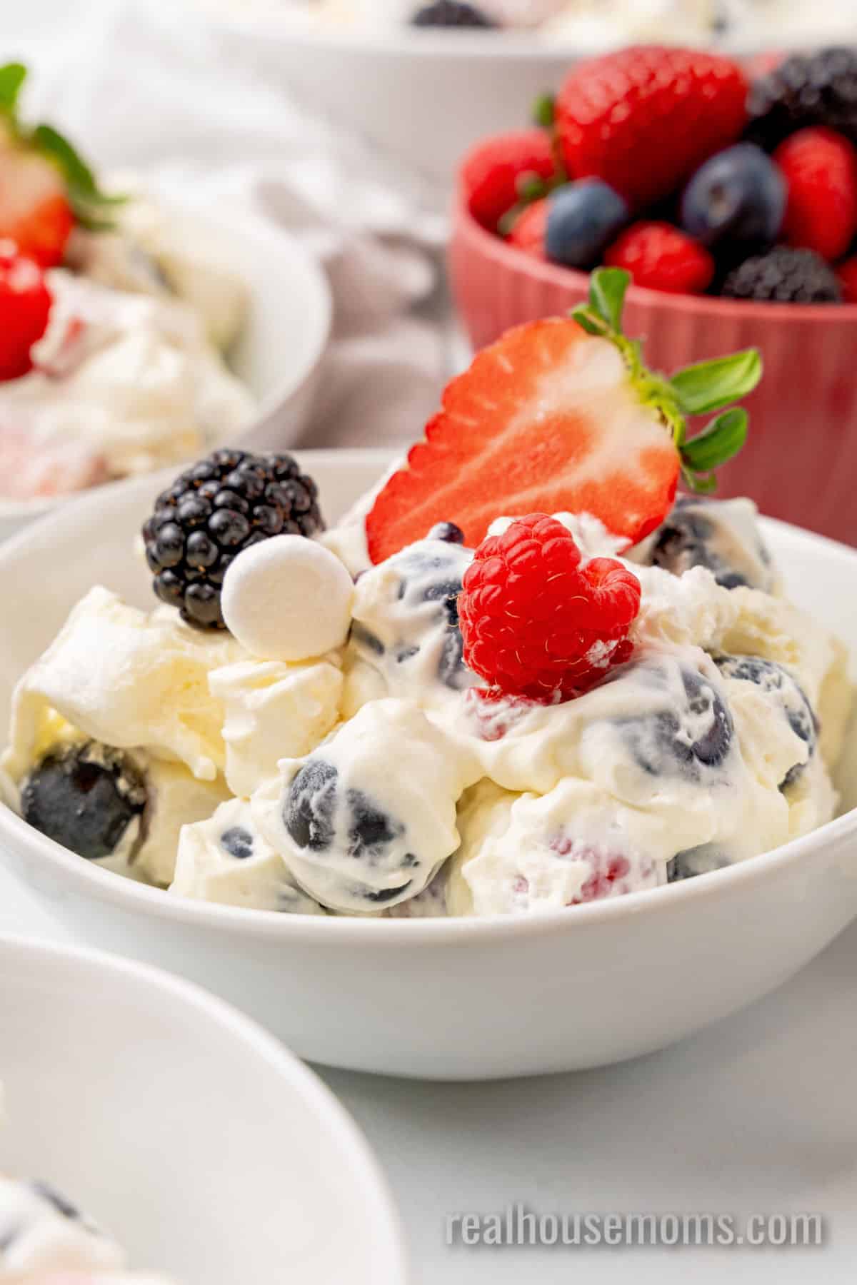 side view of a portion of red white and blue cheesecake salad topped with half of a strawberry in a small bowl