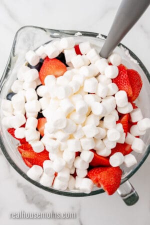 berries and mini marshmallows added to lemon cheesecake mousse in a glass mixing bowl