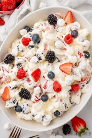 red white and blue cheesecake salad topped with more fresh berries and mini marshmallows in a serving bowl