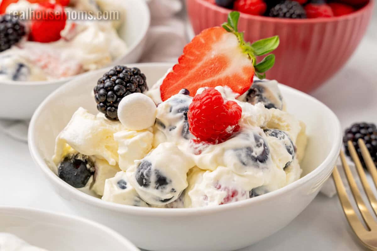 portion of red white and blue cheesecake salad topped with a strawberry half in a bowl