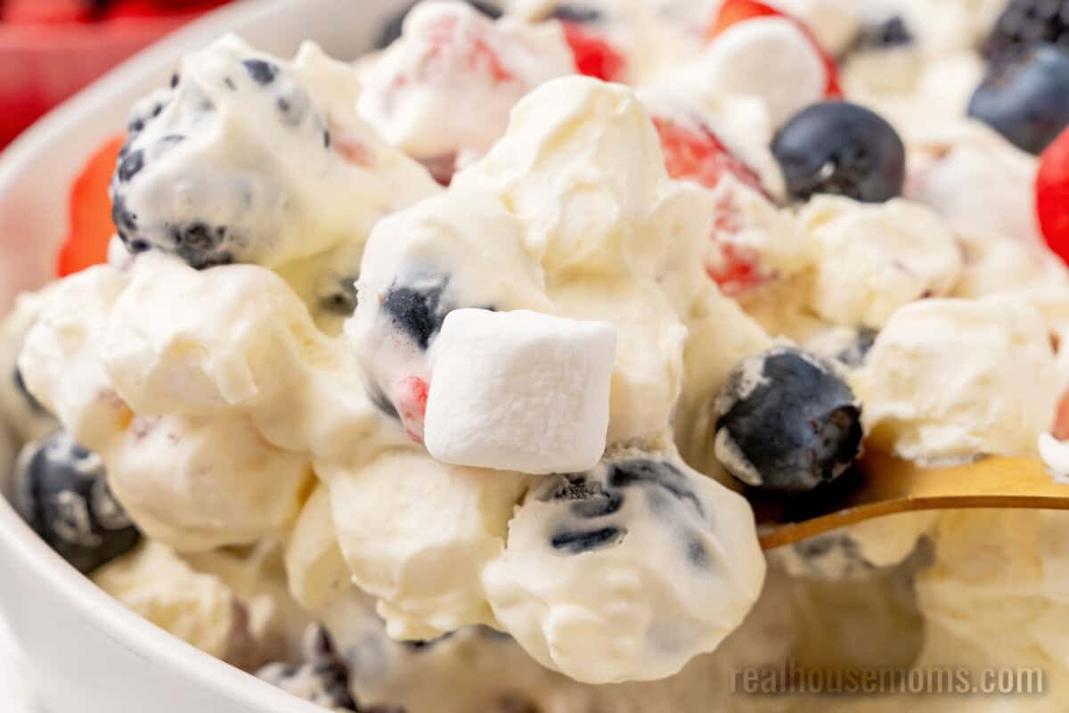 close up of a spoonful of red white and blue cheesecake salad over the serving bowl