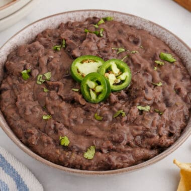 square image of refried black beans in a serving bowl topped with jalapeno and cilantro