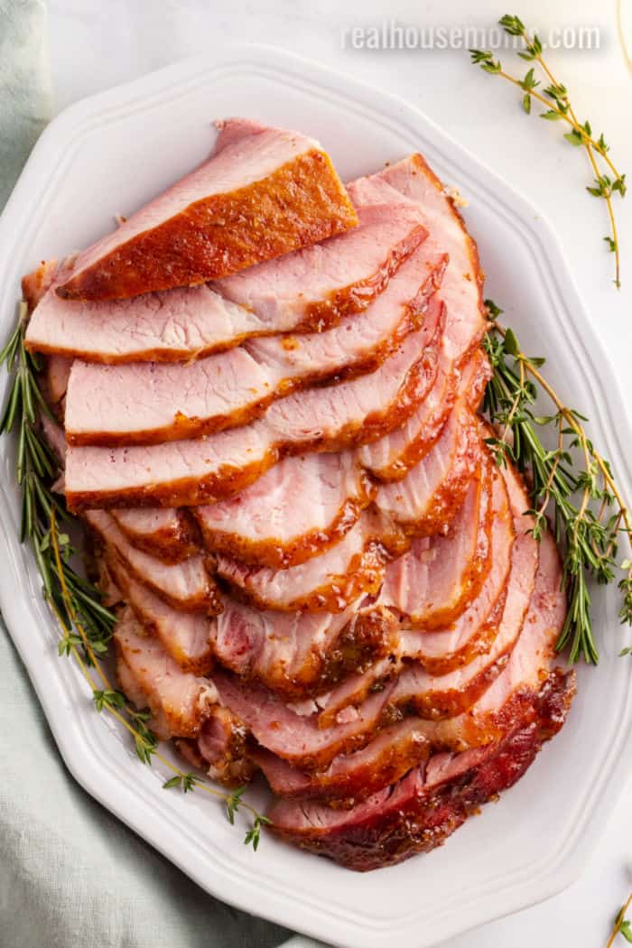reisling peach glazed ham sliced on a serving platter with thyme sprigs