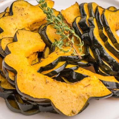 square image of roasted acorn squash slice on a plate with fresh thyme