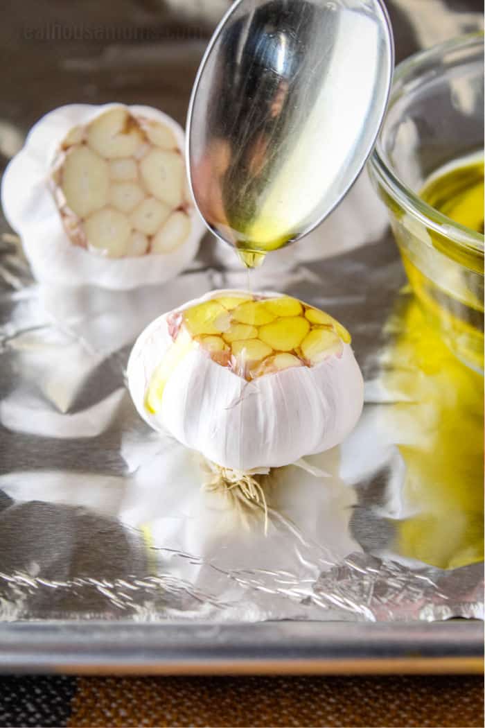 olive oil being drizzled over a head of garlic on foil