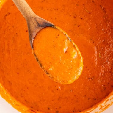 square image of roasted red pepper sauce on a wooden spoon over the skillet