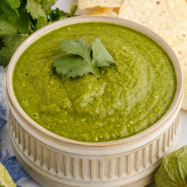 square image of roasted tomatillo salsa in a dip bowl with a sprig of cilantro on top