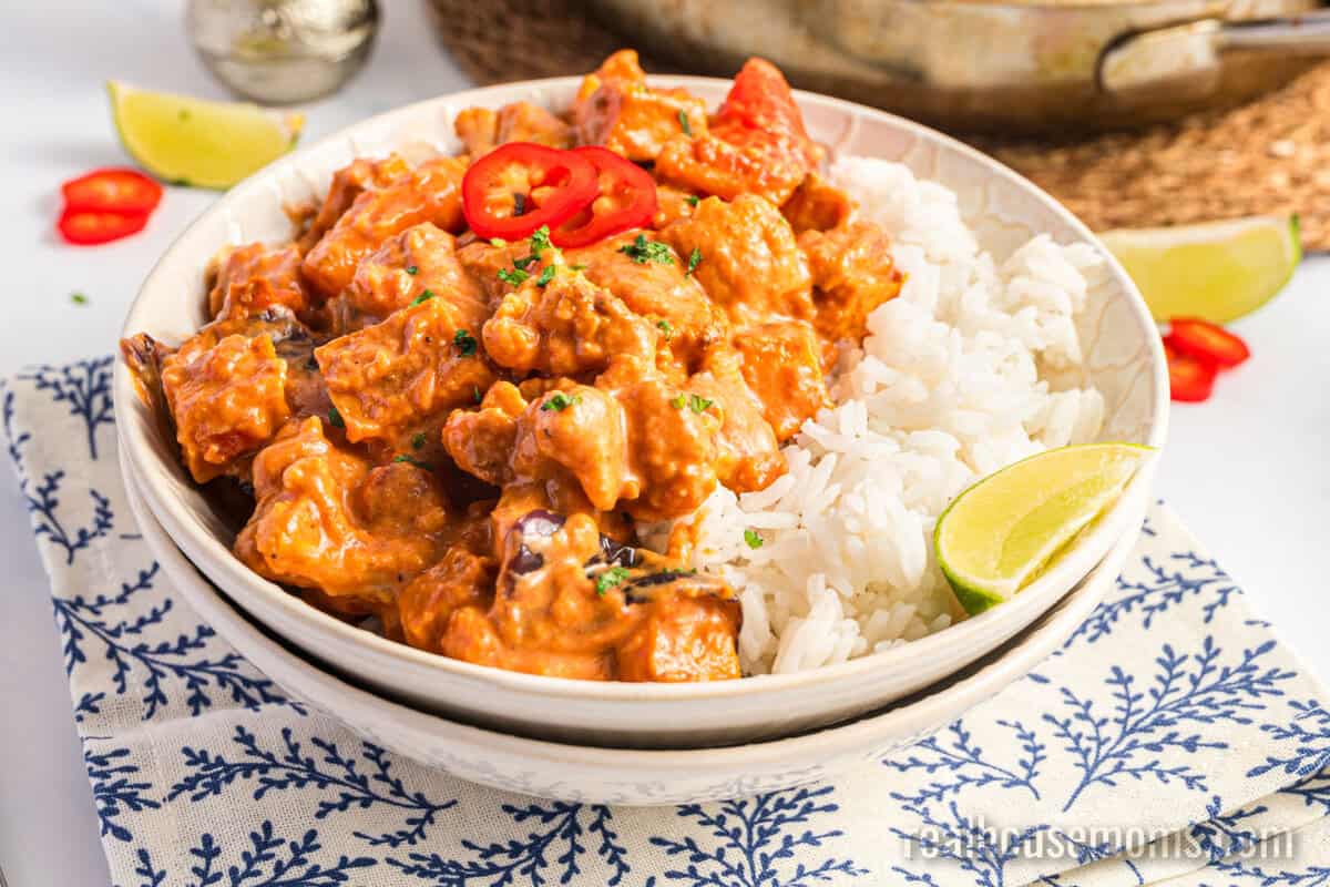 angle view of roasted vegetable curry and white rice in a bowl with lime wedges