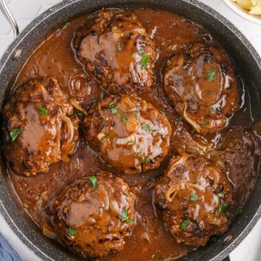 square image of Salisbury steak with onion gravy topped with chopped parsley in a skillet