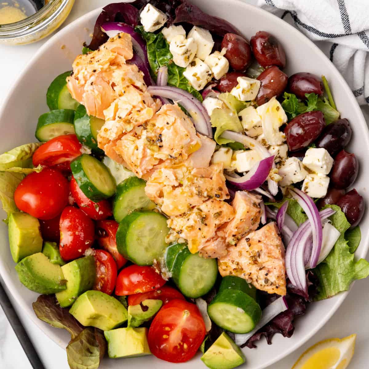 square image of a salmon salad in a bowl next to lemon wedges