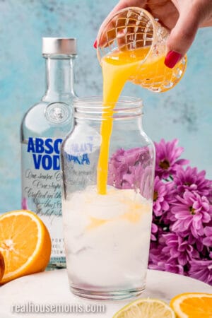 orange juice being poured into a cocktail shaker with vodka and peach schnapps