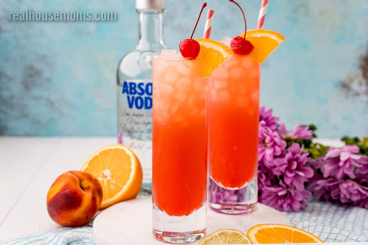 two sex on the beach drinks in front on a bottle of vodka