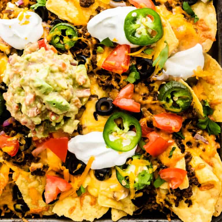 square close up image of sheet pan machos with guacamole and sour cream
