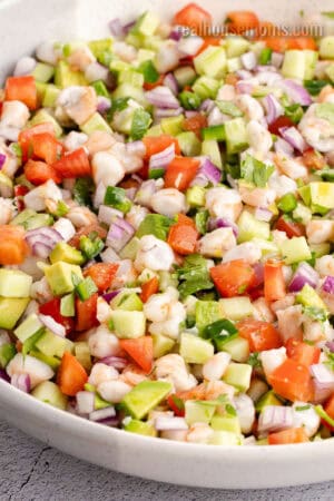 angled view of shrimp ceviche in a white bowl after being mixed