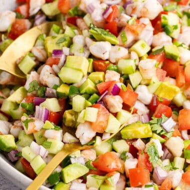 square image of shrimp ceviche in a serving bowl with gold serving spoons