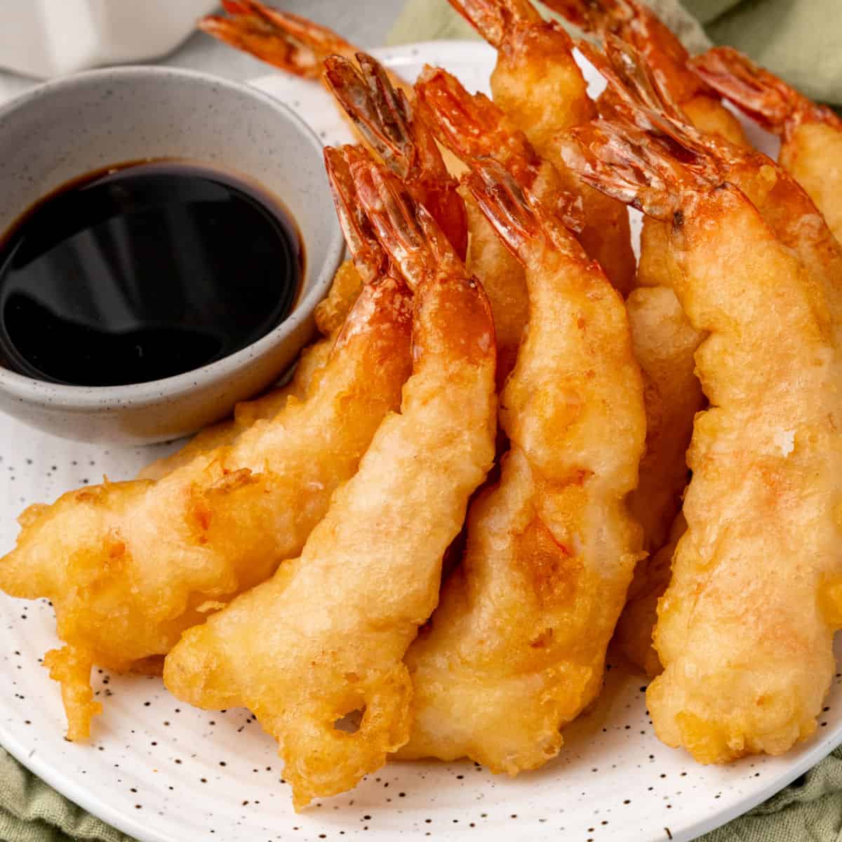 square image of shrimp tempura arranged on a plate next to a bowl of dipping sauce