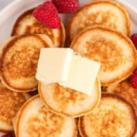 image of pile of silver dollar pancakes on a plate with pats of butter and fresh raspberries with the title of the post on top with pink and black lettering