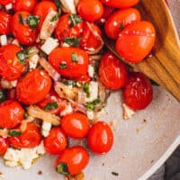 blistered tomatoes in a skillet with w wooden spoon with recipe name at the bottom