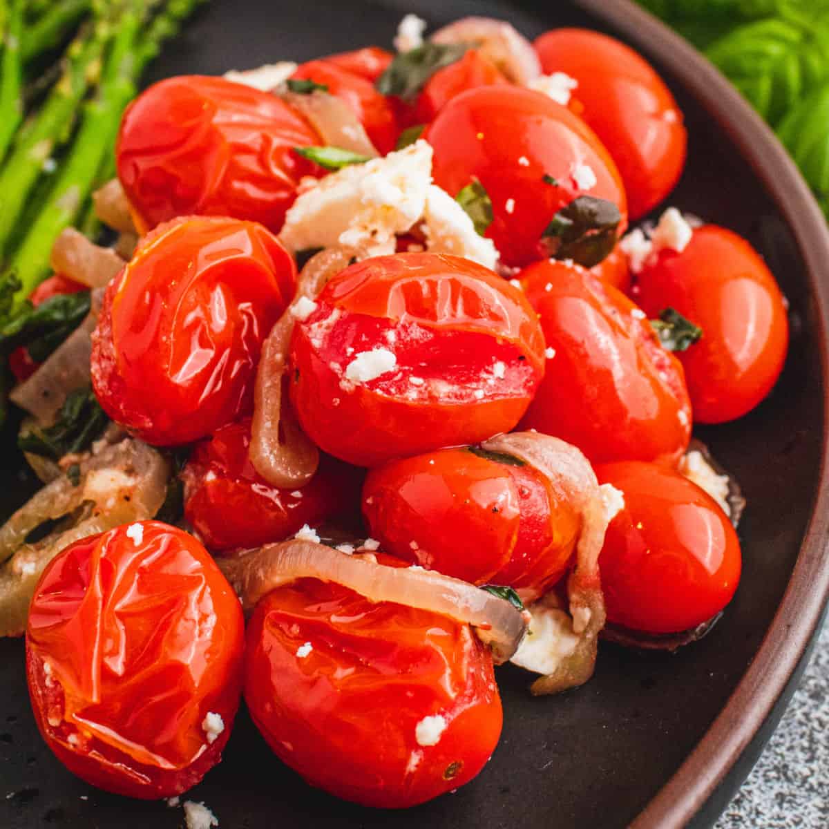 square close up image of blistered tomatoes on a plate with asparagus