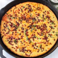 square image of pancetta corn casserole in a cast iron skillet with basil on top