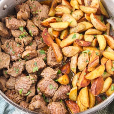 square image of skillet steak bites with potatoes with chopped parsley on top