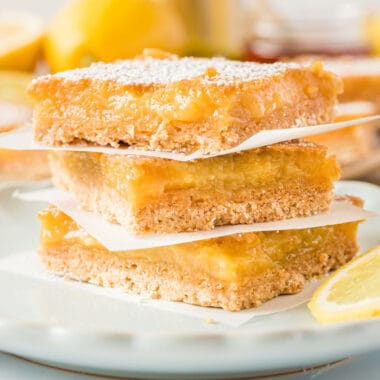 square image of skinny honey lemon bars stacked up with a piece of parchment paper between each bar
