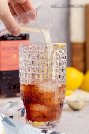 lemon juice being poured into a cocktail shaker with ice and sloe gin