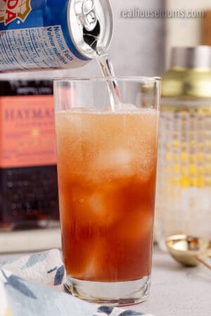 club soda being poured into a tall glass to make a sloe gin fizz