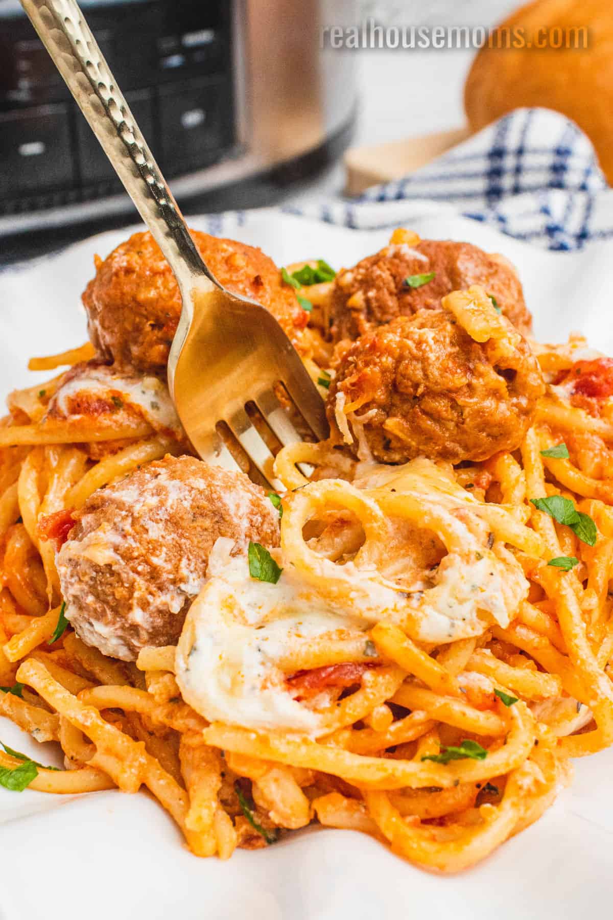 fork stabbed into a portion of Slow Cooker Cheesy Spaghetti and Meatballs on a white dinner plate
