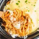 square image of a spoonful of slow cooker cheesy spaghetti and meatballs resting in the crock pot