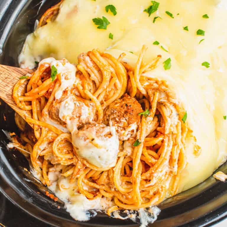 square image of a spoonful of slow cooker cheesy spaghetti and meatballs resting in the crock pot