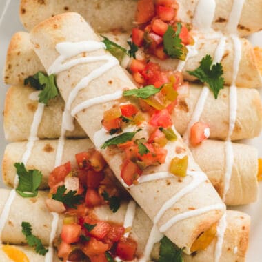 square image of chicken taquitos pield on a plate with sour cream and salsa over top