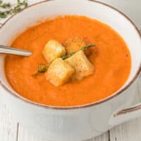 square image of slow cooker tomato soup in a bowl with a spoon garnished with croutons and fresh thyme